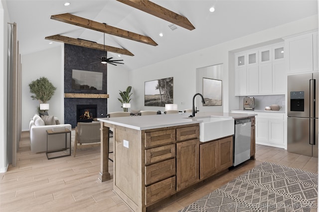 kitchen featuring appliances with stainless steel finishes, white cabinets, glass insert cabinets, and an island with sink