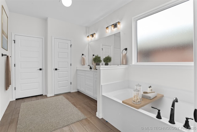 full bath featuring wood finish floors, a garden tub, vanity, and baseboards