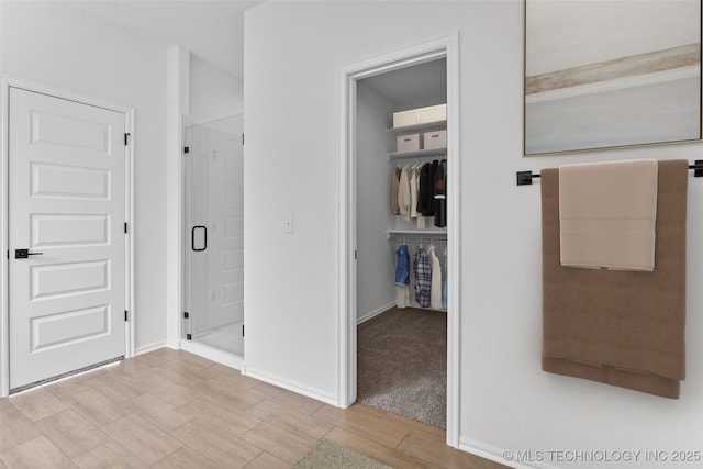 bathroom with a walk in closet, wood finish floors, and baseboards