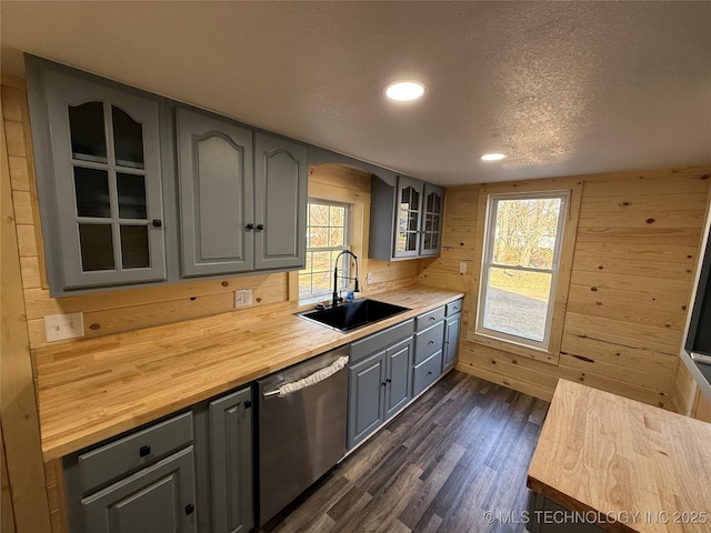 kitchen with butcher block countertops, glass insert cabinets, a sink, gray cabinetry, and stainless steel dishwasher