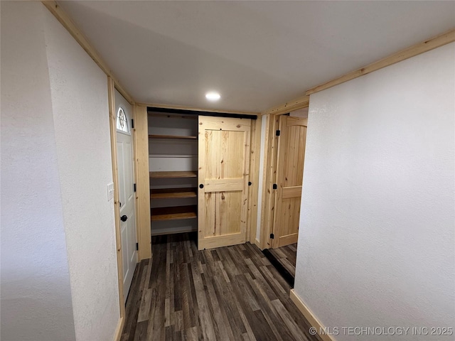 hallway featuring a textured wall, dark wood-style flooring, and baseboards