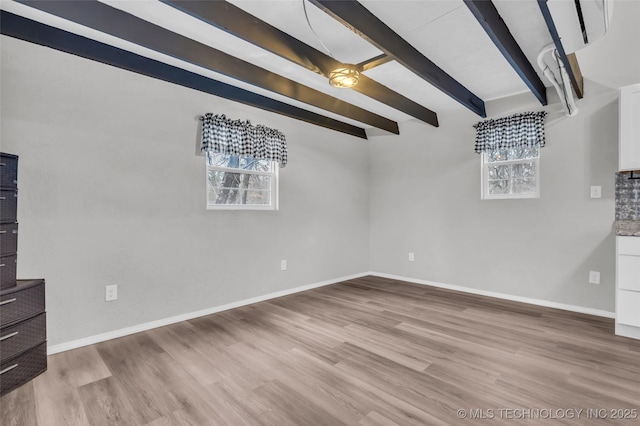 interior space featuring baseboards, beamed ceiling, and light wood finished floors