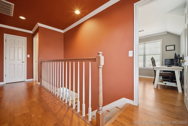 corridor with wood finished floors, an upstairs landing, visible vents, baseboards, and crown molding