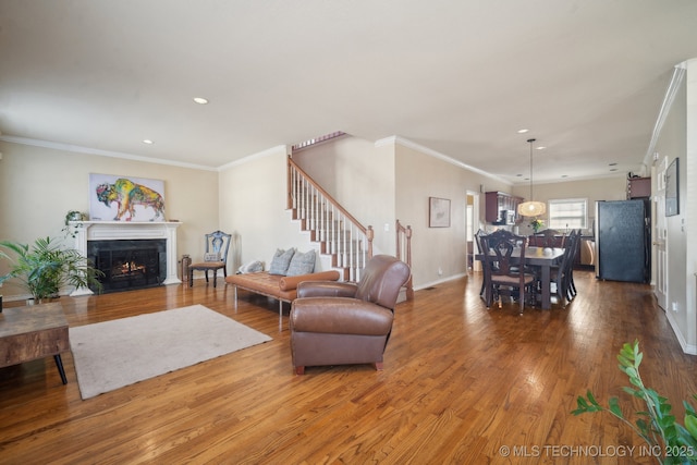 living room with recessed lighting, a fireplace with flush hearth, wood finished floors, baseboards, and ornamental molding