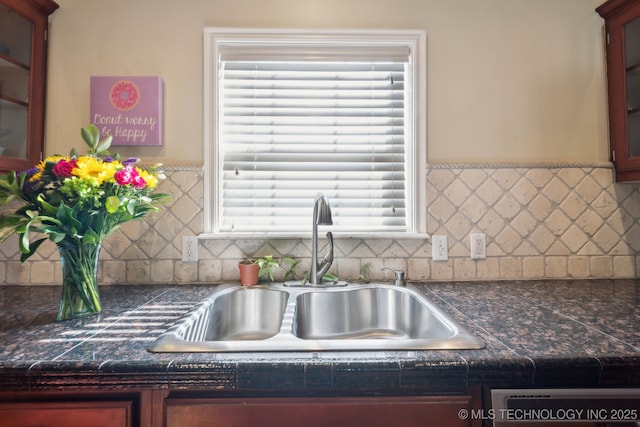 kitchen with decorative backsplash, a sink, glass insert cabinets, and dark countertops
