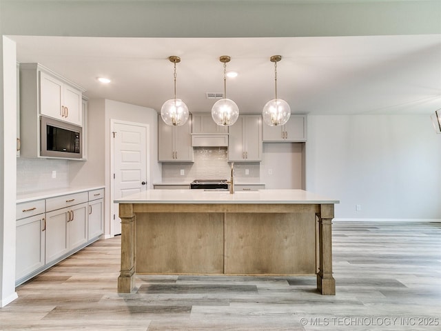 kitchen featuring black microwave, light countertops, a kitchen island with sink, and decorative light fixtures