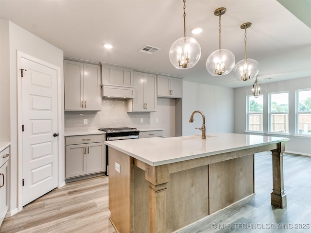 kitchen with an island with sink, light countertops, a sink, and hanging light fixtures