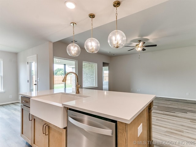 kitchen featuring pendant lighting, a center island with sink, light countertops, stainless steel dishwasher, and a sink