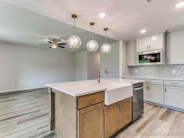 kitchen with dishwasher, a kitchen island with sink, built in microwave, light countertops, and a sink