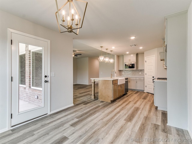 kitchen with decorative light fixtures, a center island with sink, light wood finished floors, light countertops, and built in microwave