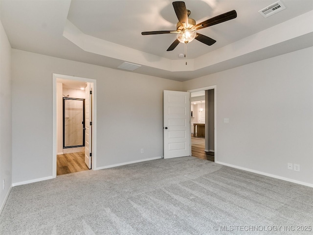 unfurnished bedroom with light carpet, a raised ceiling, visible vents, and baseboards