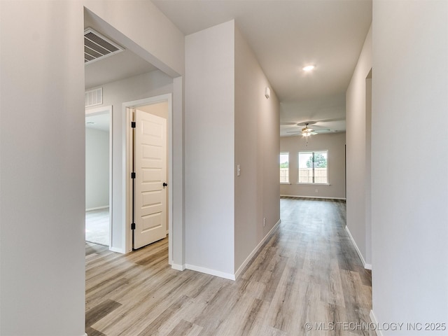 corridor with light wood finished floors, baseboards, and visible vents