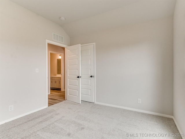 unfurnished room featuring baseboards, lofted ceiling, visible vents, and light colored carpet