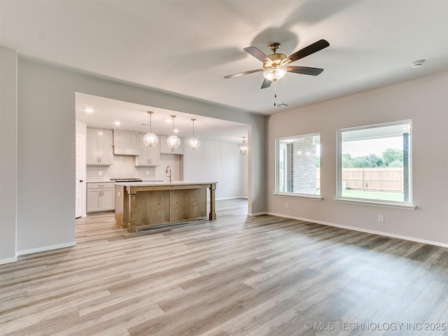 unfurnished living room featuring baseboards, a sink, a ceiling fan, and light wood-style floors