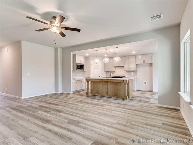 kitchen with visible vents, white cabinetry, light countertops, built in microwave, and a center island with sink