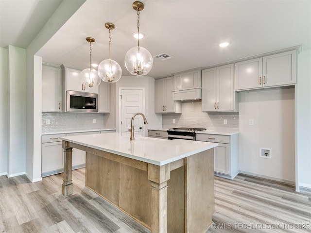 kitchen featuring a kitchen island with sink, a sink, stainless steel range oven, light countertops, and built in microwave