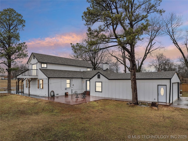 back of property at dusk featuring a garage, a shingled roof, a lawn, and a balcony