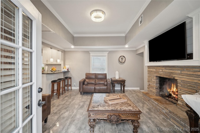 living room featuring a fireplace, a raised ceiling, visible vents, ornamental molding, and baseboards