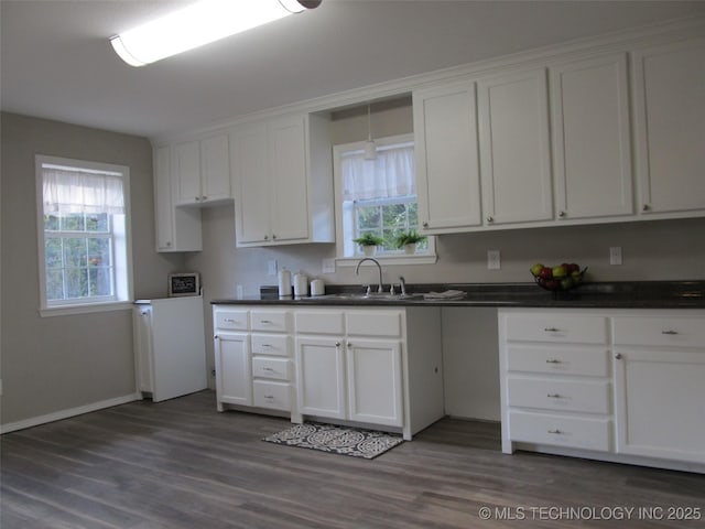 kitchen with dark countertops, a sink, white cabinetry, and dark wood-type flooring