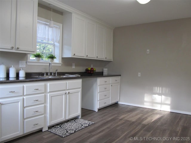 kitchen featuring dark countertops, white cabinetry, dark wood-style flooring, and a sink