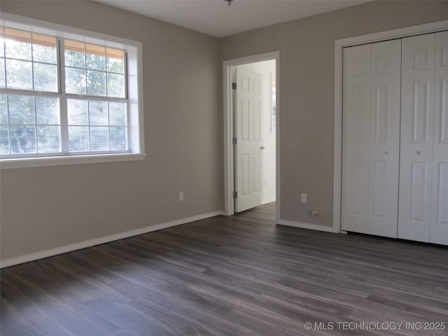 unfurnished bedroom with dark wood-style floors, a closet, and baseboards