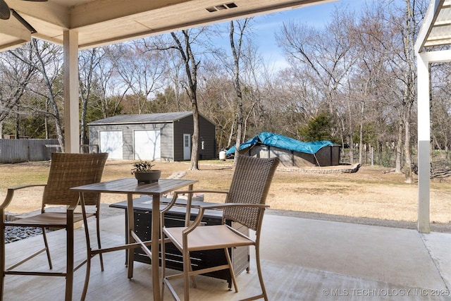 view of patio / terrace featuring an outbuilding, a garage, fence, visible vents, and a storage unit