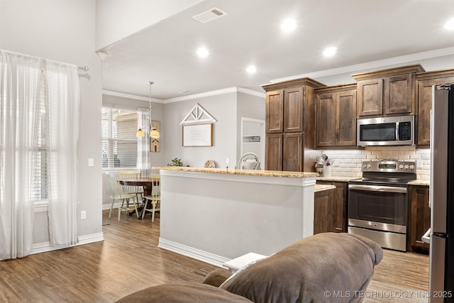 kitchen with appliances with stainless steel finishes, decorative backsplash, decorative light fixtures, and light wood-style floors