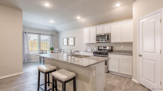 kitchen featuring light stone counters, a kitchen island with sink, a sink, white cabinets, and appliances with stainless steel finishes