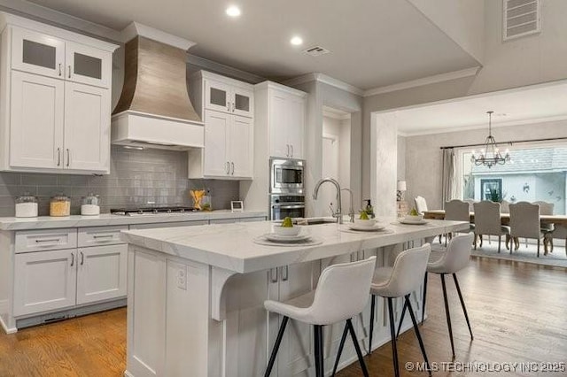 11904 S Toledo Ave, Tulsa, OK 74137 - kitchen featuring an island with sink, custom range hood, glass insert cabinets, and stainless steel appliances
