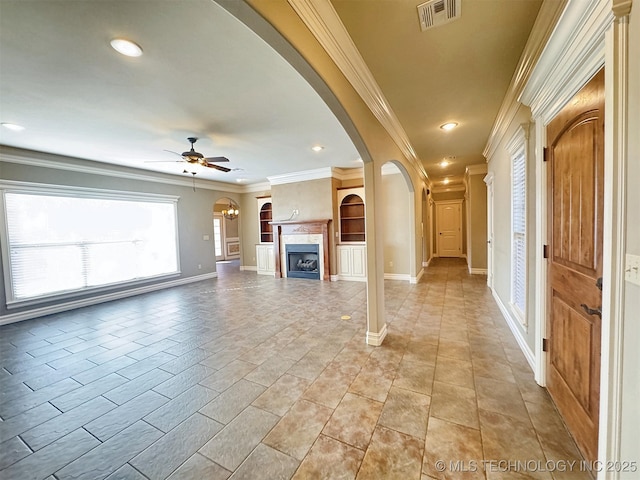 unfurnished living room with arched walkways, crown molding, a fireplace, visible vents, and ceiling fan