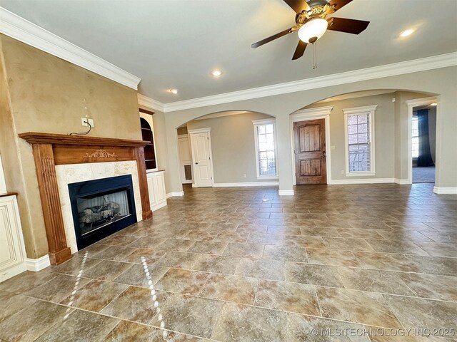 unfurnished living room with crown molding, arched walkways, a tile fireplace, and baseboards