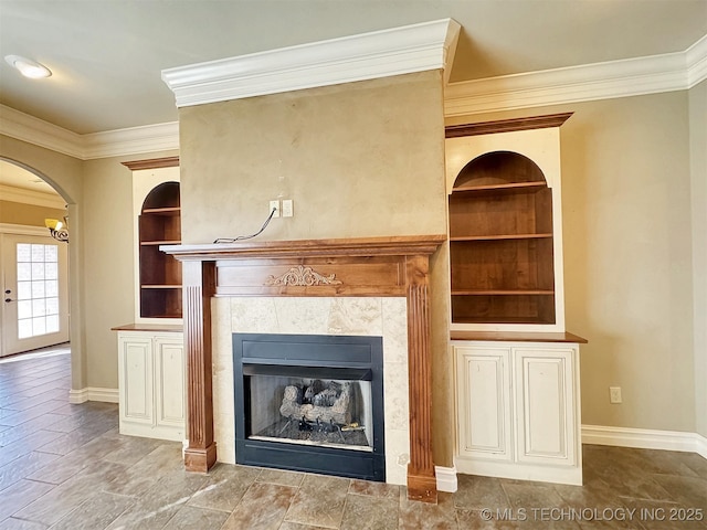 unfurnished living room featuring baseboards, built in shelves, arched walkways, and a fireplace