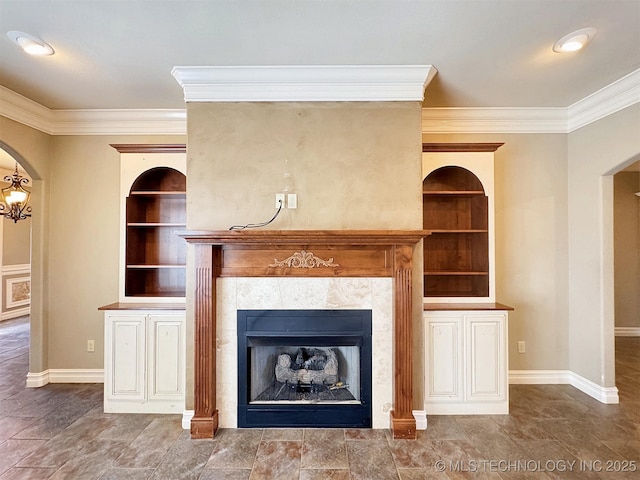 unfurnished living room with built in features, arched walkways, a fireplace, ornamental molding, and baseboards