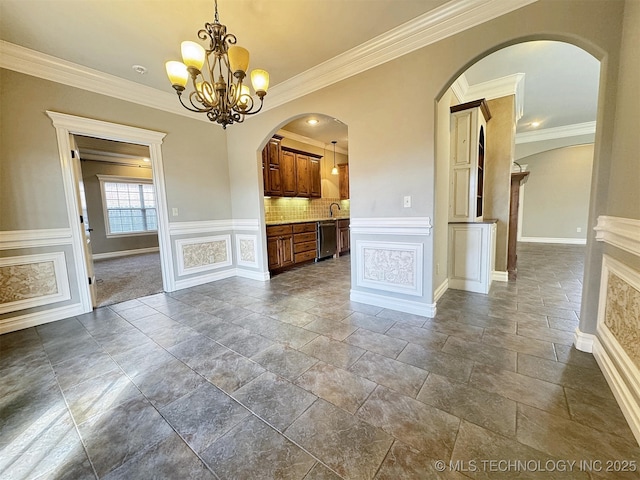 interior space with crown molding, a decorative wall, a sink, and an inviting chandelier