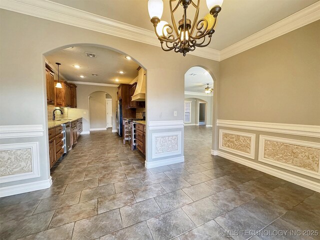 interior space featuring light stone counters, crown molding, custom exhaust hood, appliances with stainless steel finishes, and a sink