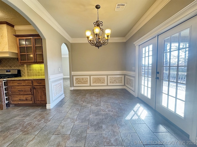 unfurnished dining area featuring visible vents, a decorative wall, crown molding, and french doors