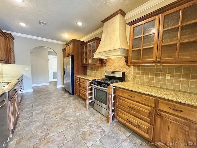 kitchen featuring arched walkways, custom range hood, visible vents, decorative backsplash, and appliances with stainless steel finishes