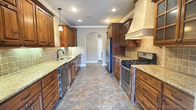 kitchen with baseboards, arched walkways, stainless steel appliances, premium range hood, and a sink