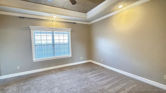 carpeted spare room with a tray ceiling, crown molding, baseboards, and ceiling fan