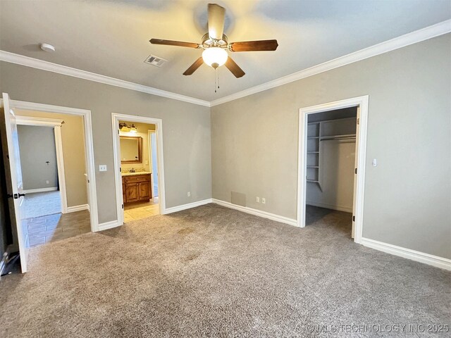 unfurnished bedroom with baseboards, visible vents, light colored carpet, ornamental molding, and a walk in closet