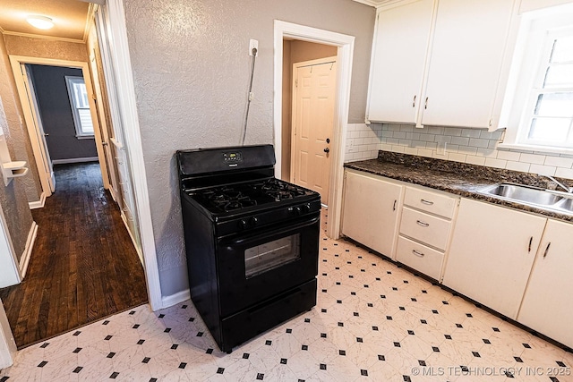 kitchen featuring a sink, white cabinets, black range with gas stovetop, light floors, and dark countertops