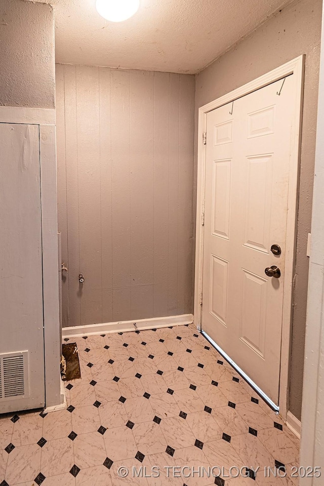 doorway to outside featuring a textured ceiling, wood walls, and tile patterned floors