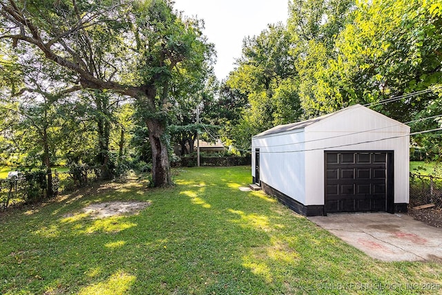 view of yard with concrete driveway, a detached garage, fence, and an outdoor structure