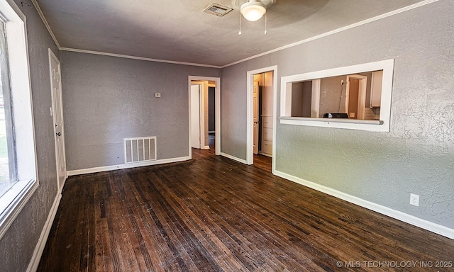 empty room featuring a textured wall, dark wood-type flooring, visible vents, and crown molding