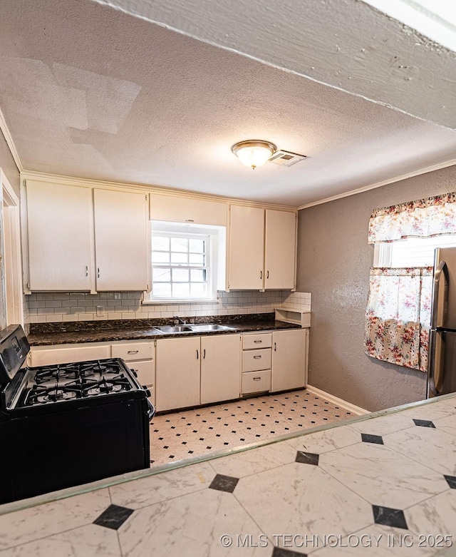 kitchen featuring dark countertops, a textured wall, backsplash, freestanding refrigerator, and black range with gas cooktop