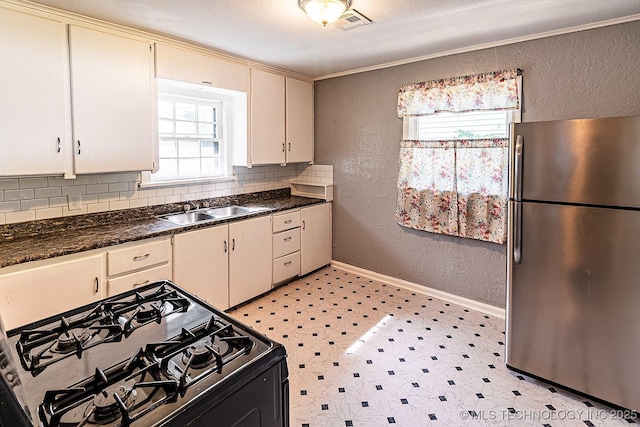 kitchen with a textured wall, decorative backsplash, freestanding refrigerator, black gas stove, and a sink