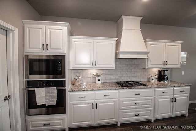 190 N Castle St, Skiatook, OK 74070 - kitchen featuring appliances with stainless steel finishes, custom range hood, white cabinets, backsplash, and light stone countertops