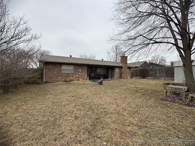 rear view of house with a yard, brick siding, and fence