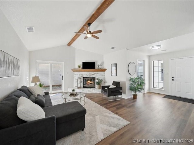 living room featuring vaulted ceiling with beams, visible vents, dark wood-style flooring, and a glass covered fireplace