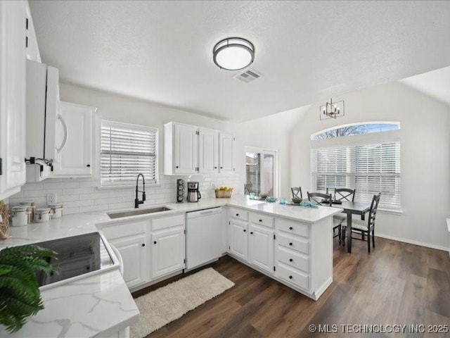 kitchen featuring lofted ceiling, a peninsula, a sink, white cabinets, and dishwasher